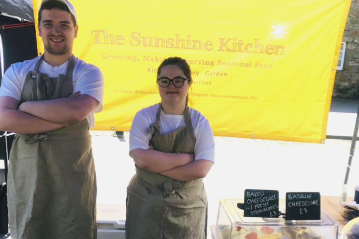 Young people standing next to a 'Sunshine Kitchen' sign with baked goods.