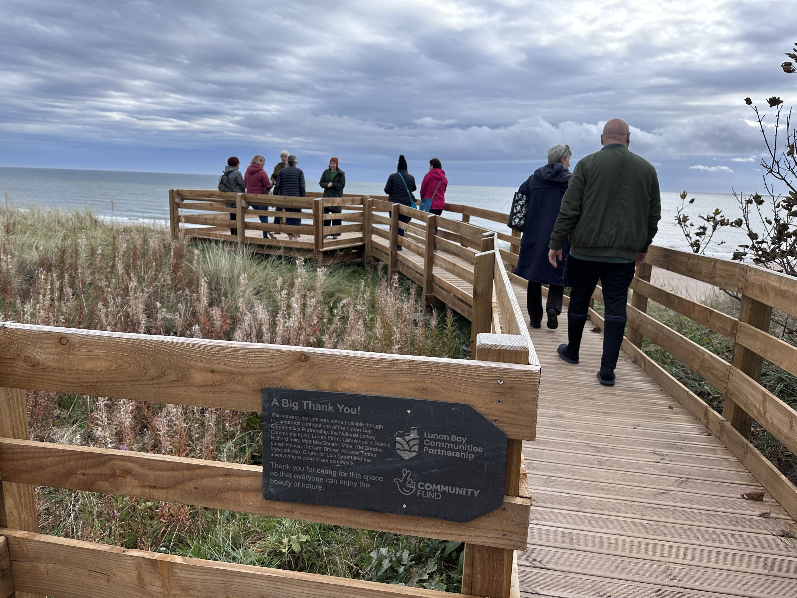 People on a wooden platform looking over Lunan Bay, Angus