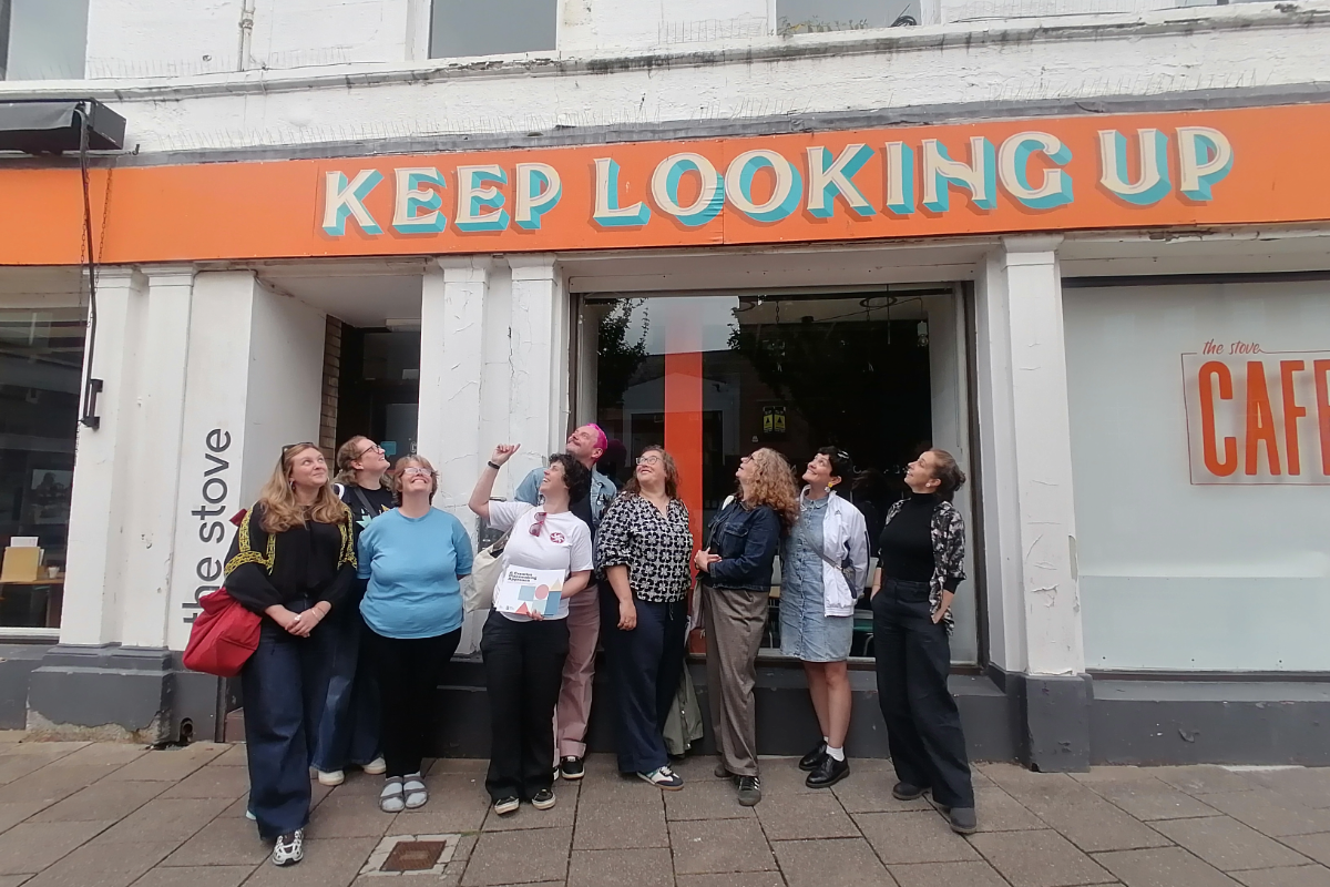 A group of people smiling looking up at a shop front sign