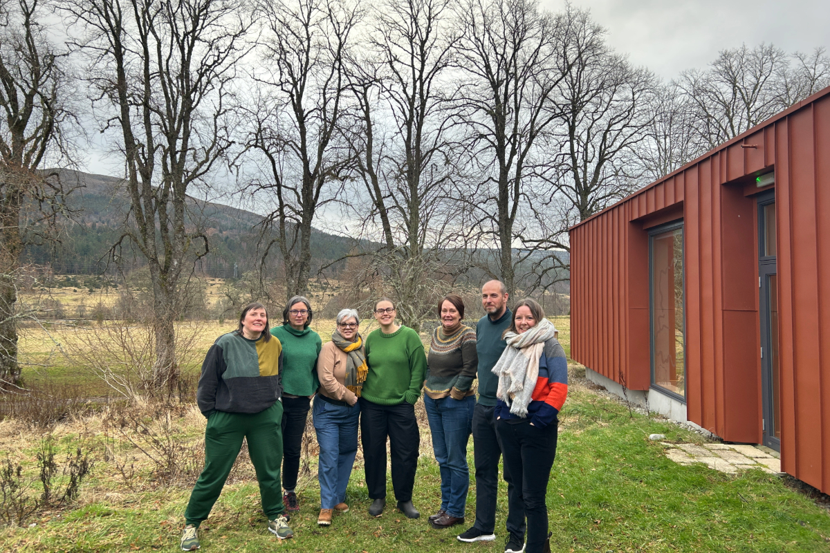 7 people standing together smiling beside a community hub with tress behind them