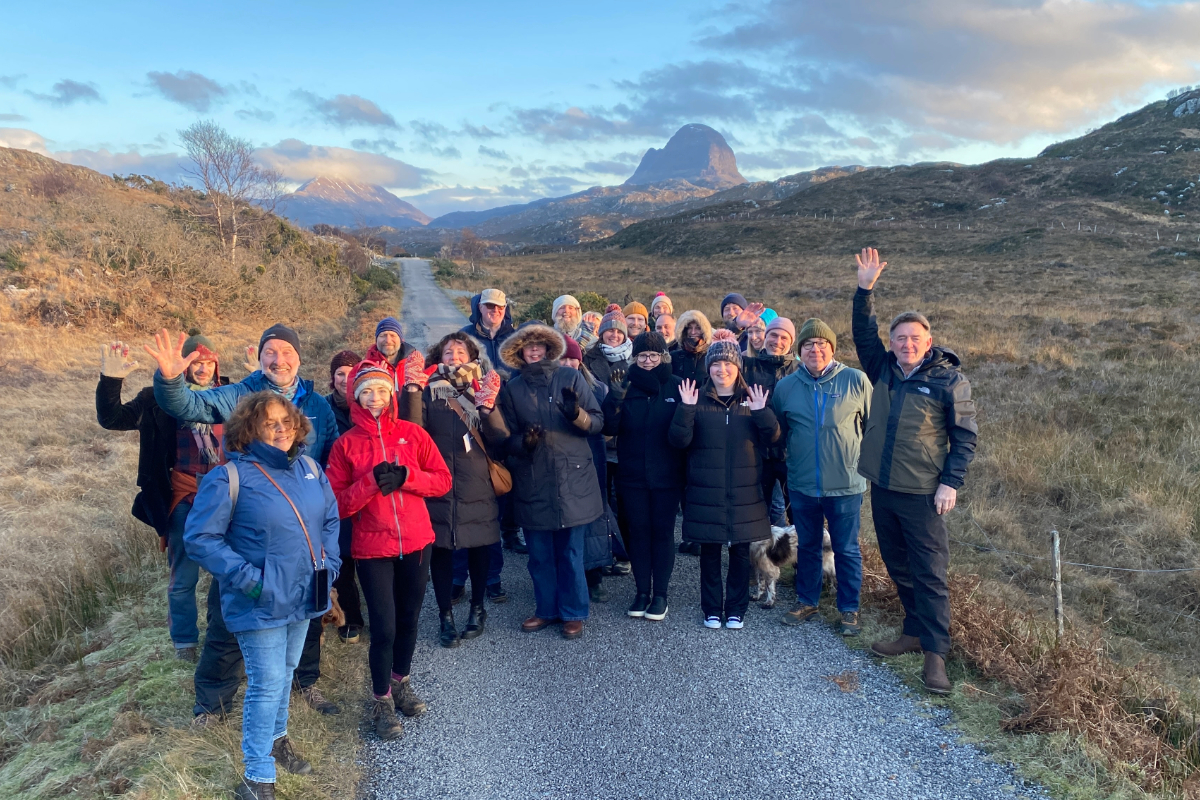 A group of people standing on a country road in Assynt with hills and mountains behind them.