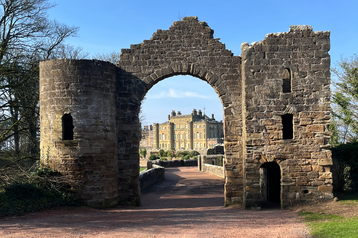Image of Culzean Castle centred through the frame of an old wall with trees and shrubs on each side