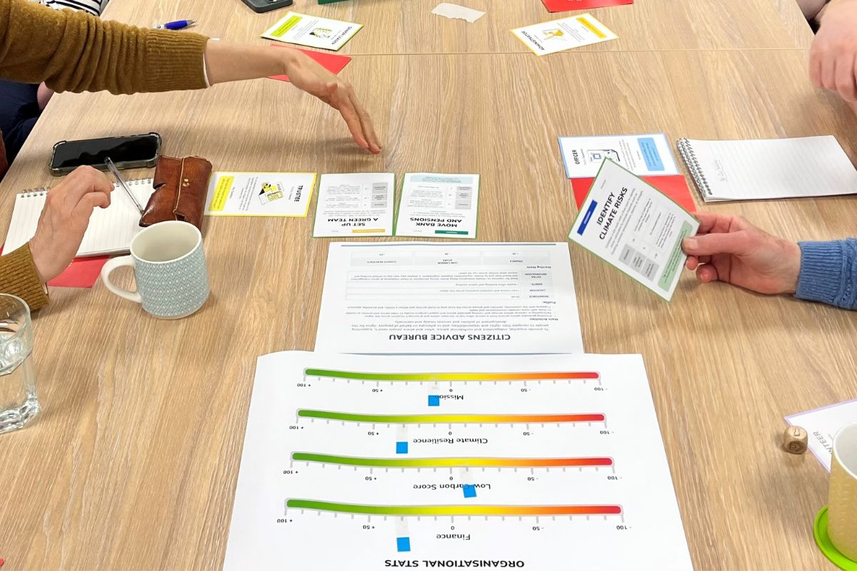 A table top, with paper and cards on top and peoples hands at either side of the table.