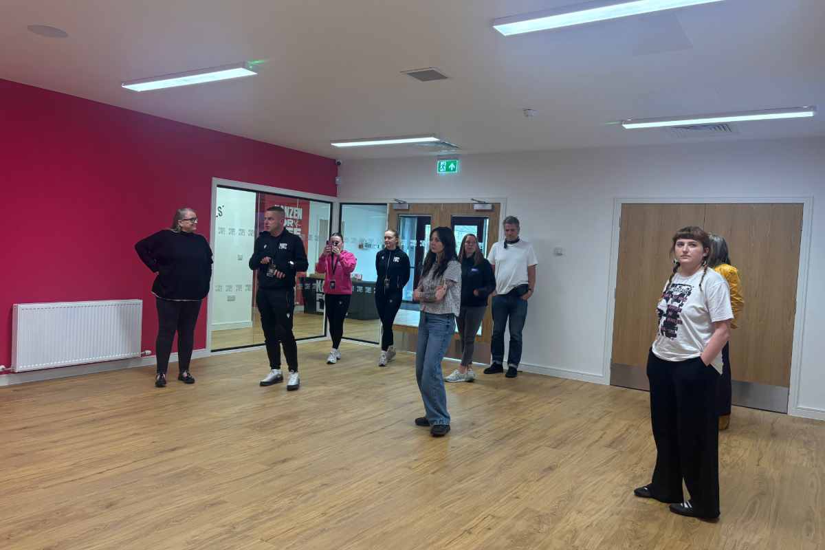 A group of 8 people standing inside a gym hall with wooden floor boards and strobe lighting